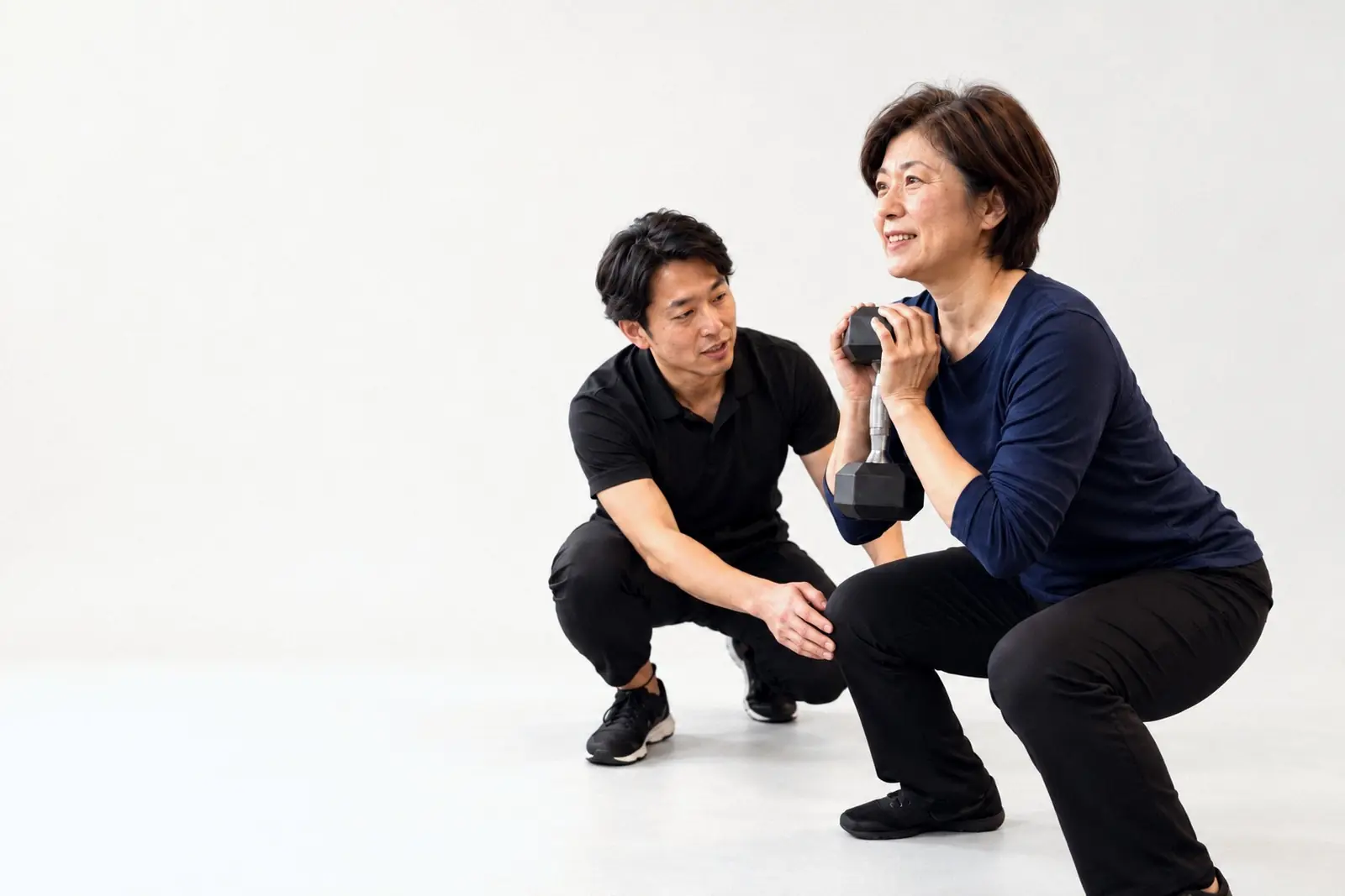 トレーナーに見守られながらスクワットをする女性